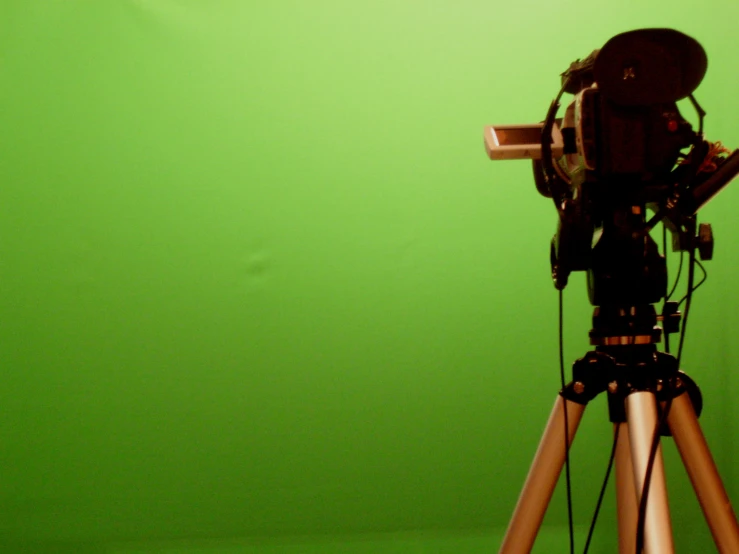 a tripod with a camera attached to it against a green background
