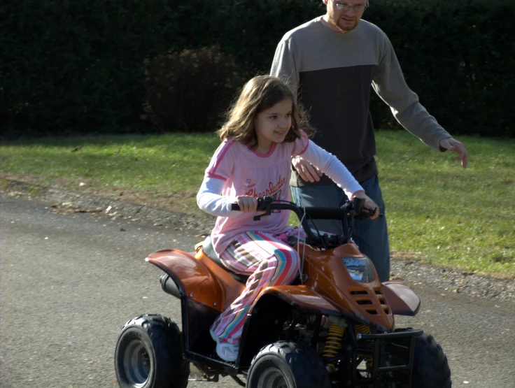 the man shows the girl how to drive a small four - wheeler