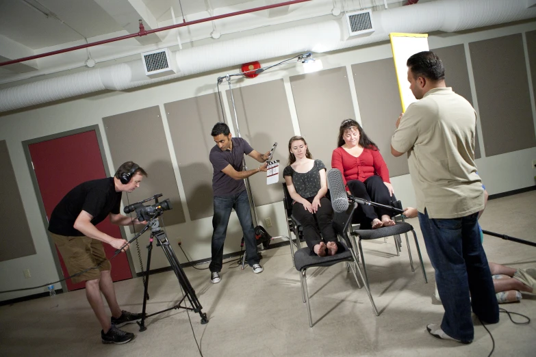 five people are sitting on chairs watching another person filming