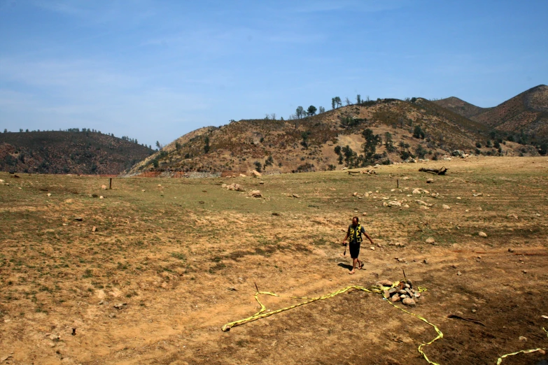 a man in the wilderness looking down at a grassy area with yellow fire hoses