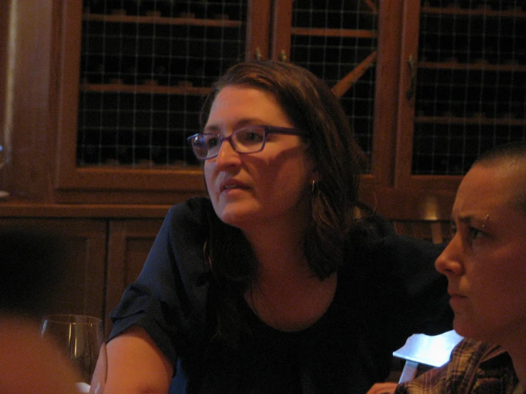 a woman sitting at a table next to another person with a glass of wine