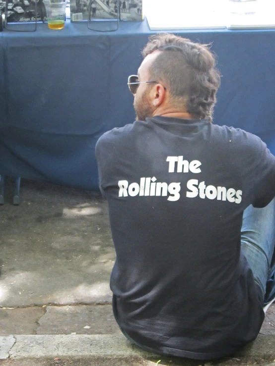 a man sitting on a bench and wearing a black shirt that reads the rolling stones