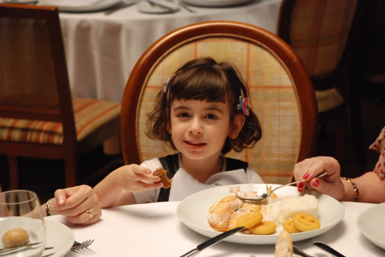 a little girl eating food while seated at a table