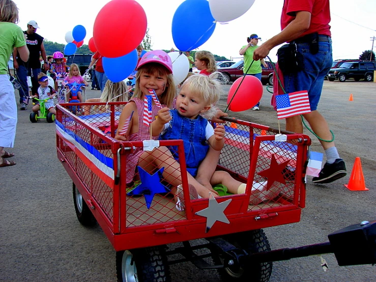 children sit in the bed of a red wagon full of balloons