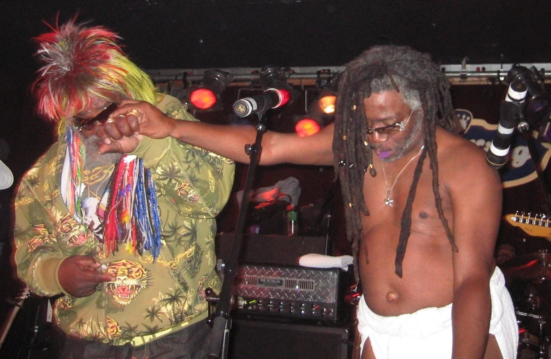 a man with dreadlocks holding onto his shirt while standing next to a musician