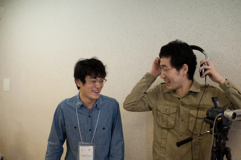 two men laughing as they hold a cell phone up to their ears