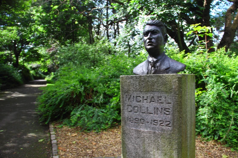 a statue sitting on the edge of a path with flowers growing by it