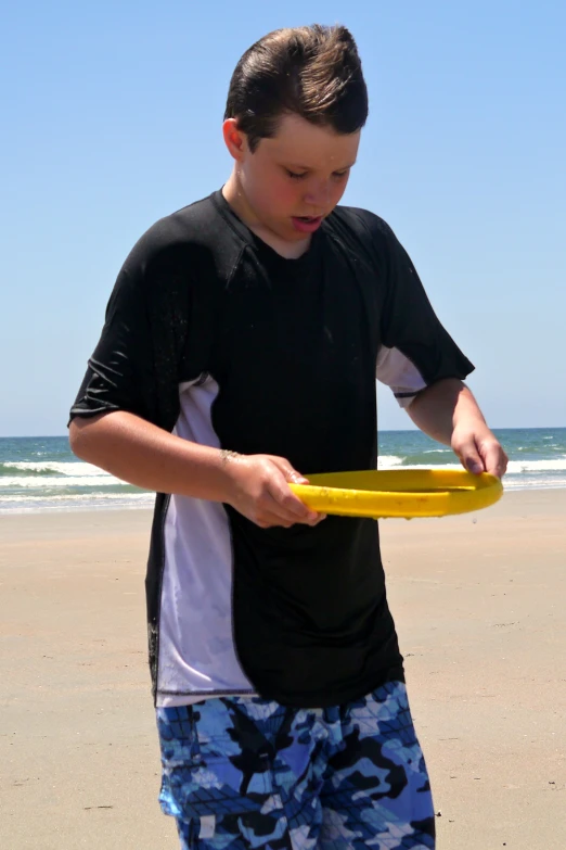 a boy standing in the sand holding a frisbee