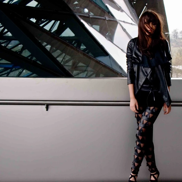 a girl with long hair standing by a wall in tight boots