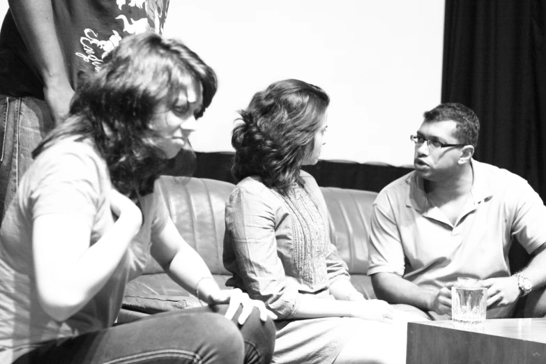 the woman is sitting with two males while the one in the white dress