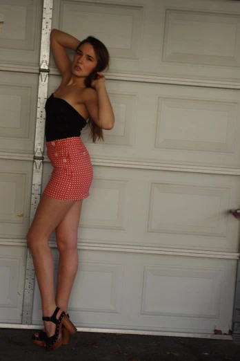 a beautiful woman leaning against a garage door wearing short shorts