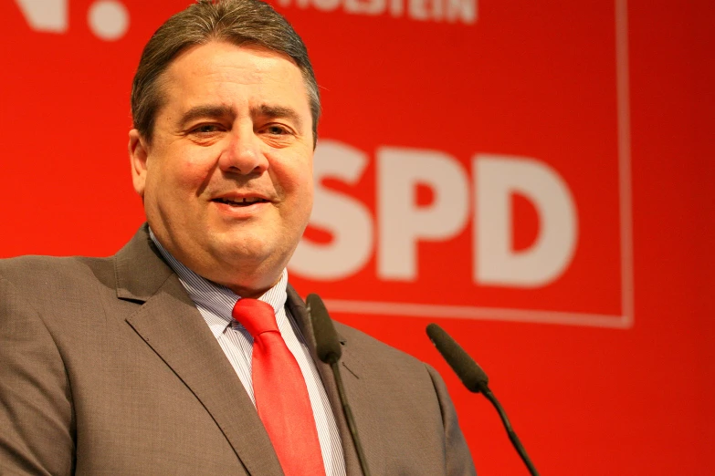 a man wearing a red tie standing in front of a microphone