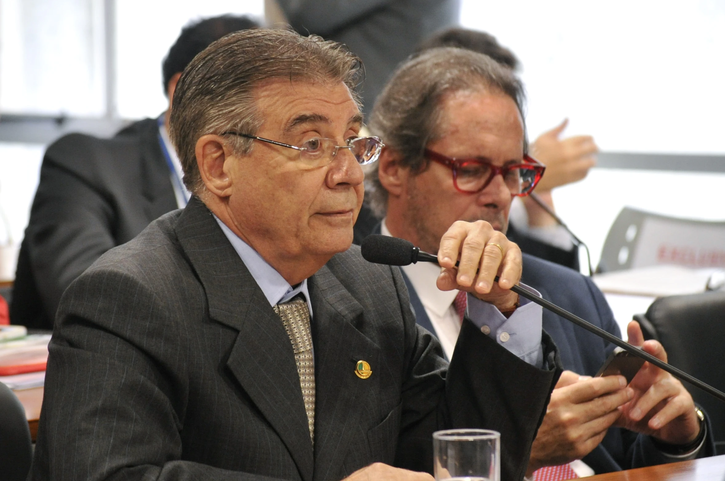 two men sit at a conference with one talking