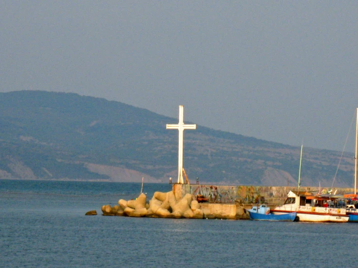 two small boats are docked near the shore with a cross on top of it