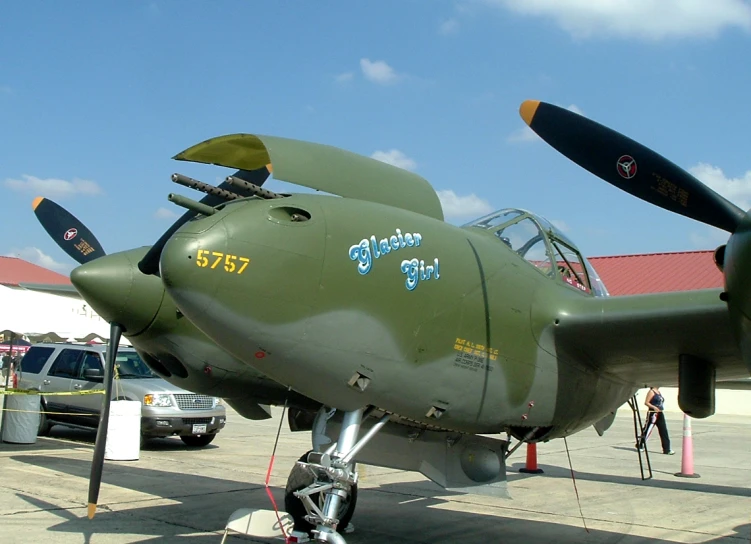 a green plane with two pilots standing in front of it