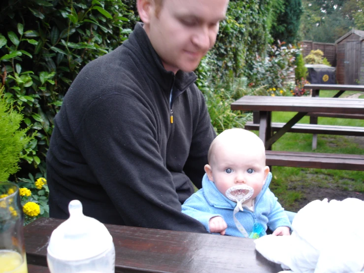 a baby boy in a blue sweater and his father outside on a picnic table