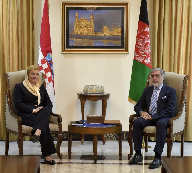 the two people are sitting in chairs, one with a gold scarf around his neck