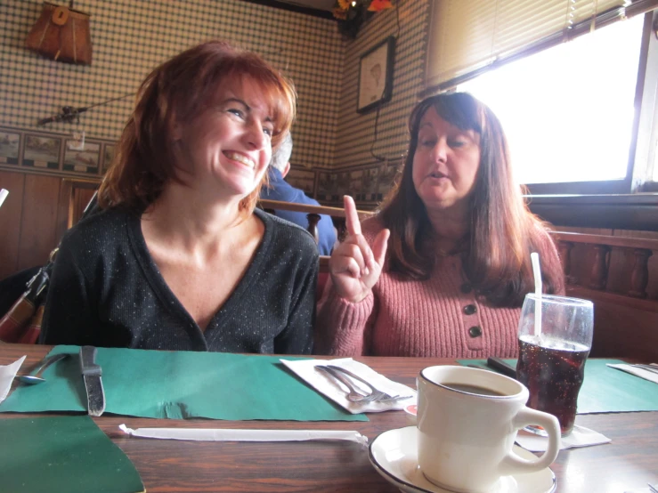 two women sitting at a table smiling and making a peace sign
