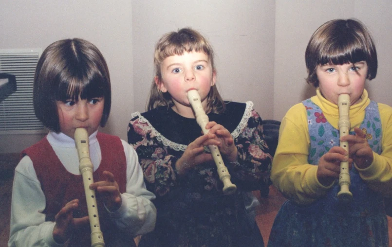 three children are playing flutes while a second  is listening