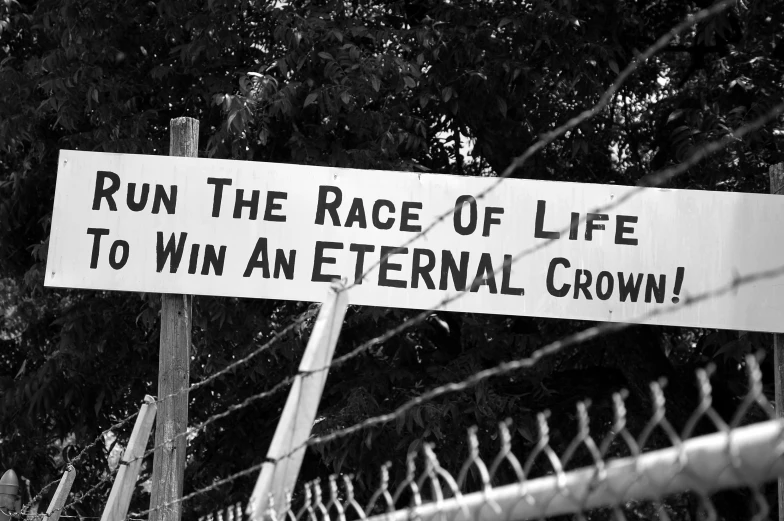 a sign posted behind some barbed wire with trees in the background