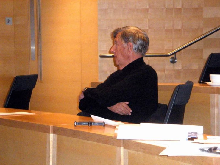 a man wearing a black shirt sitting at a desk in a room