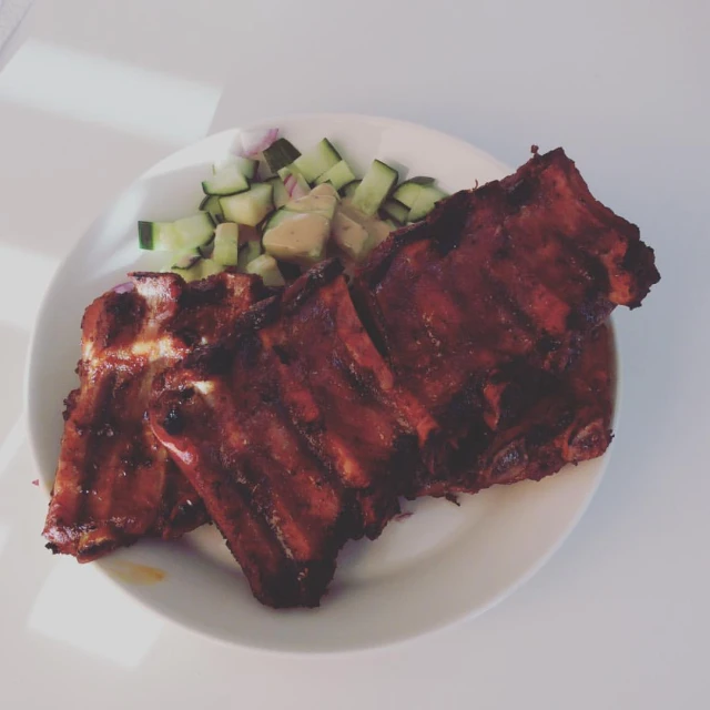 two bbq ribs with some cucumbers and sauce