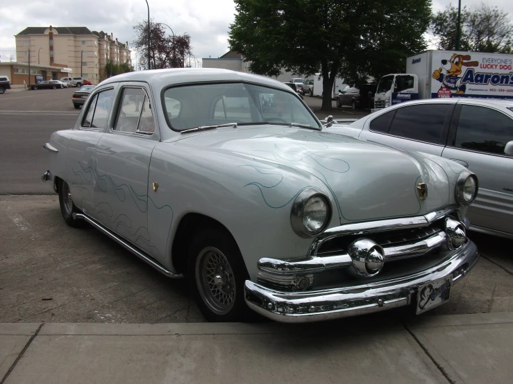 an old, grey car sits parked in a lot with another one behind