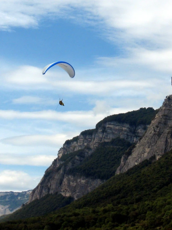 an parasailer in the air over mountains, with two parachutes in the background