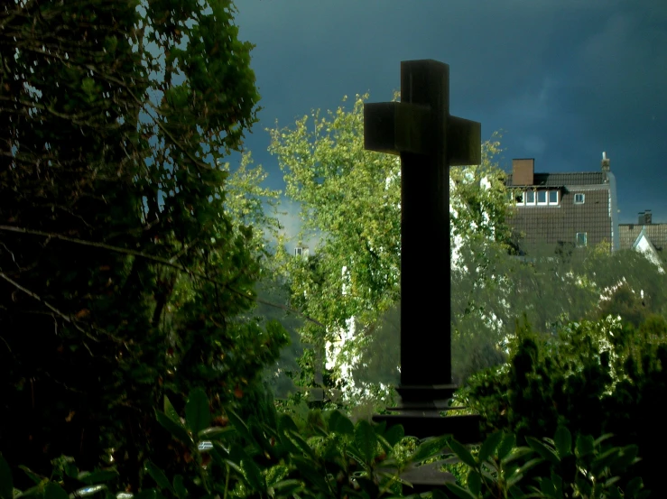 a cross standing in the foreground surrounded by greenery and trees