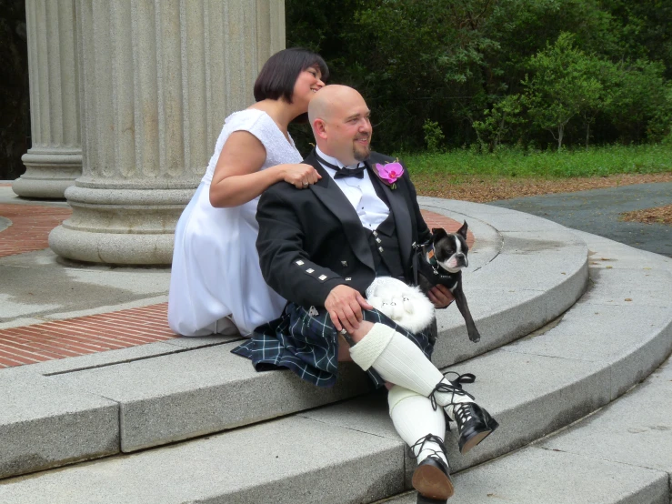 a man in a tuxedo and a woman in a white dress sitting on stairs