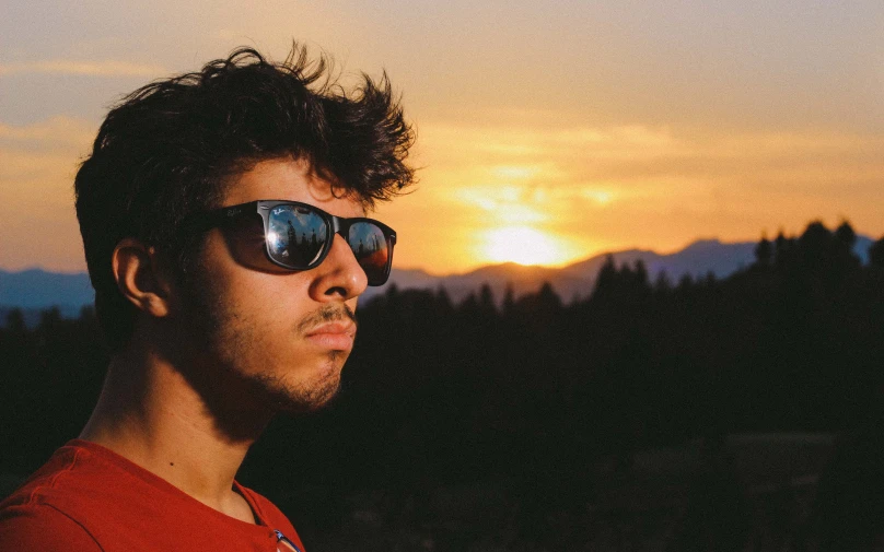 a young man with sunglasses on in front of the mountains
