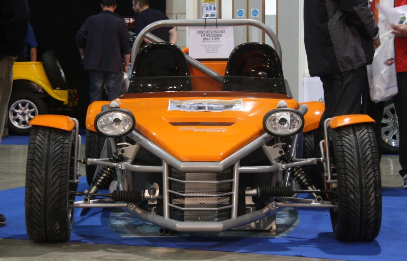 an orange vehicle with big tires on display at a car show