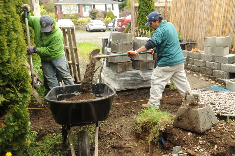 a couple of men digging in dirt to build a fence