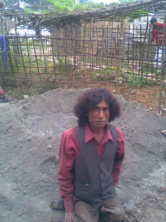 a man is sitting in a muddy area with two chickens