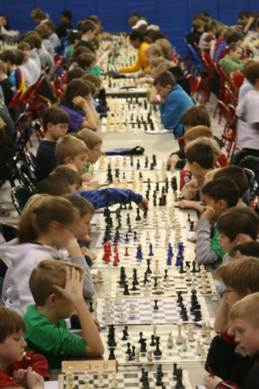 children at the chess table watch as one player moves over the chess board