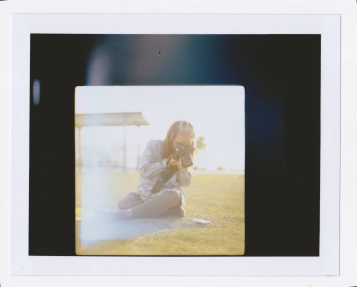 a woman kneeling in grass with a camera