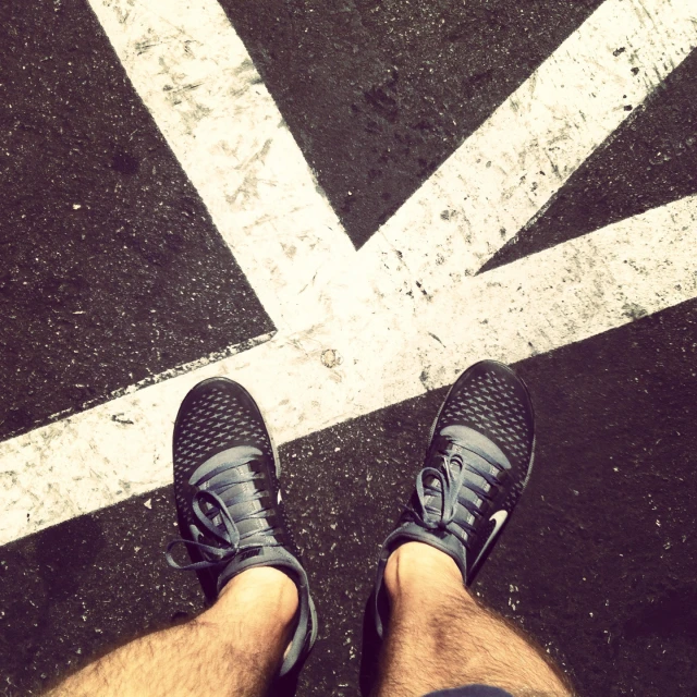 a person is wearing black sneakers and standing in a parking lot