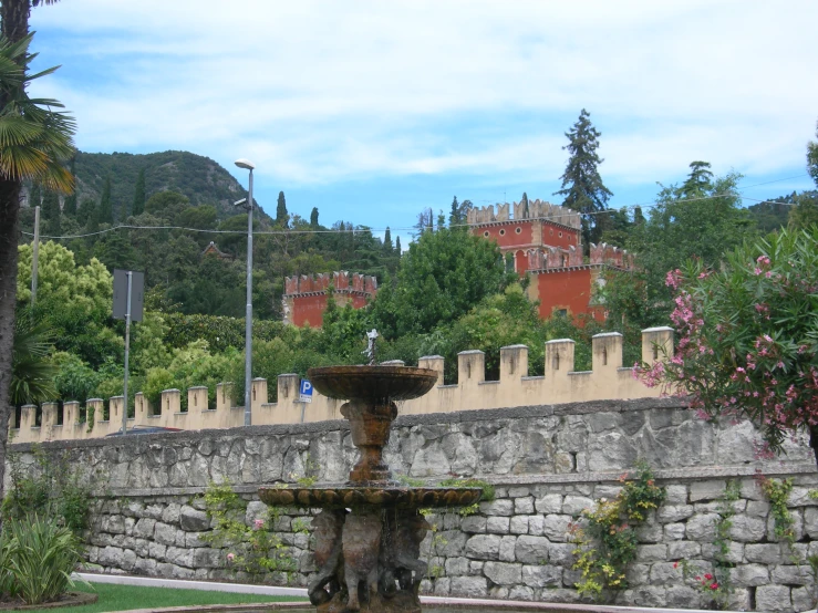 a large fountain in front of a stone wall and some trees