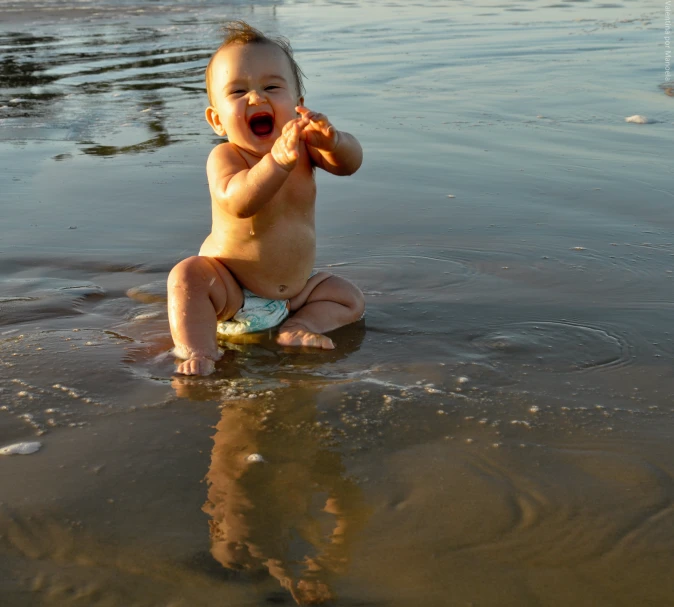 a young baby sitting on the beach playing