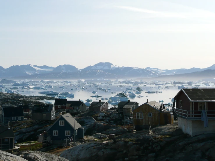 many small houses near the ocean, one has snow covered mountains