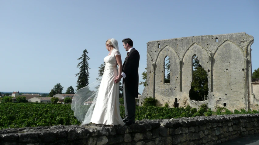 a bride and groom are on a bridge near an old castle