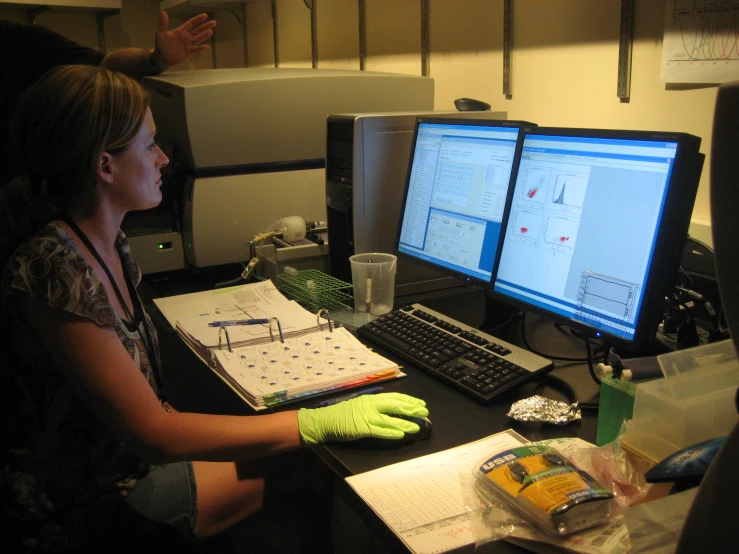 a woman sitting in front of two monitors at a desk