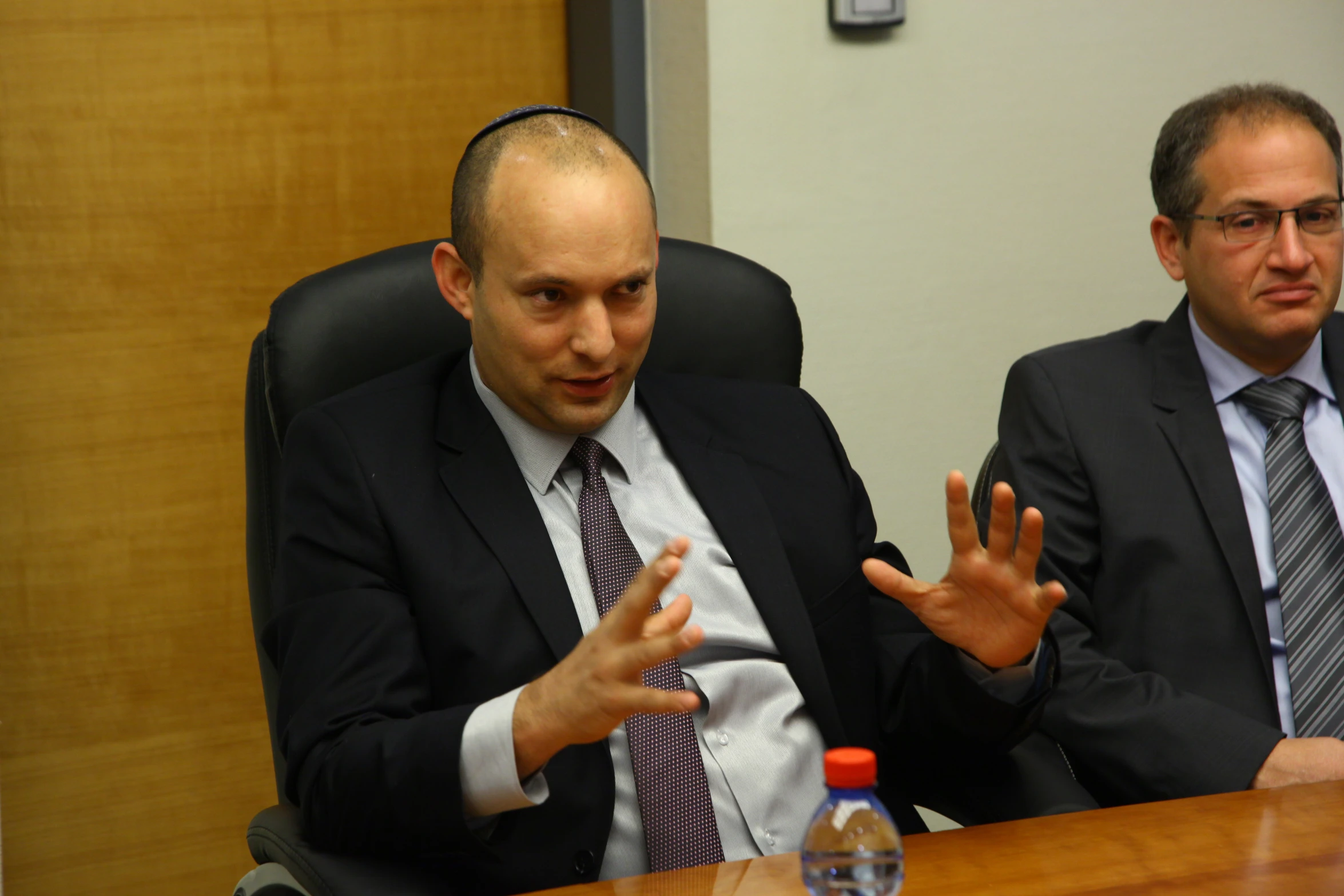 two men sitting at a desk with one gesturing