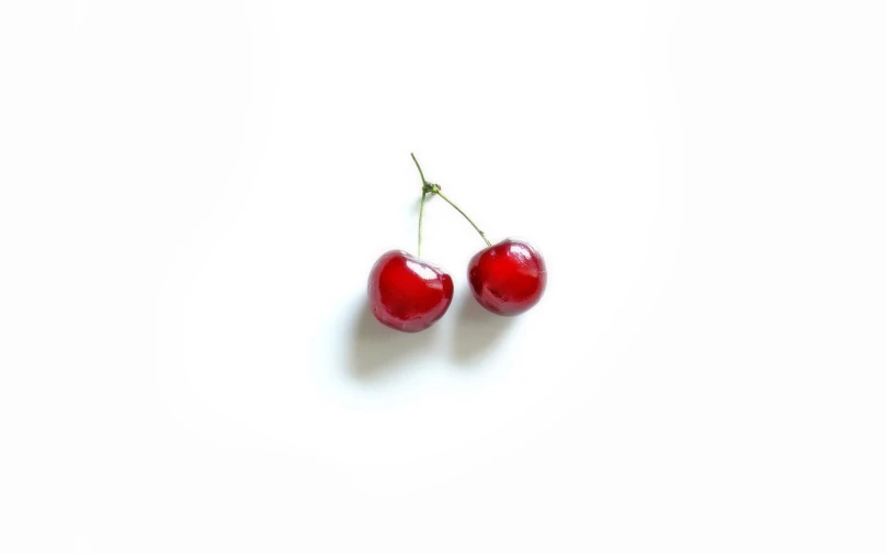 two cherries are seen on a white surface