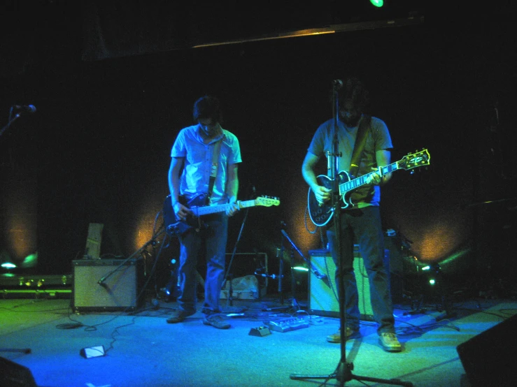 a couple of men playing guitars in a dark room