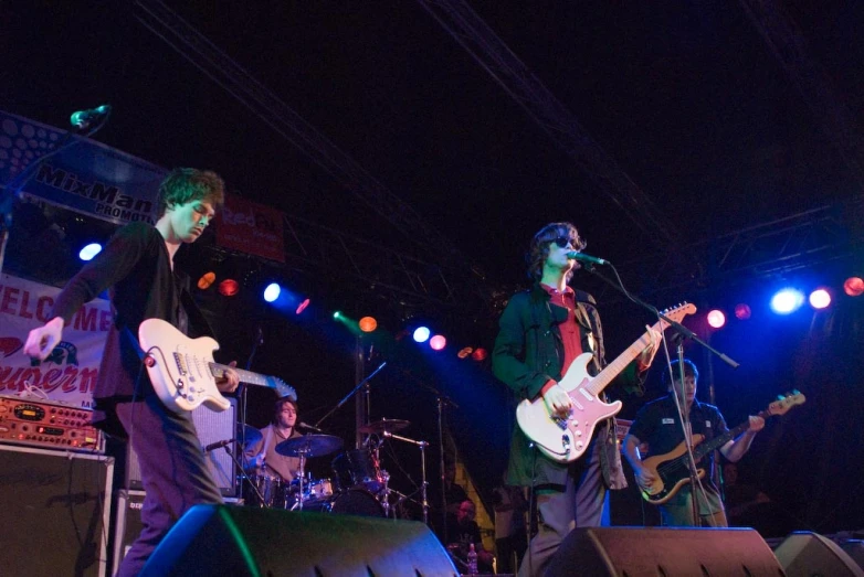 two people playing guitar on stage while others stand and sing