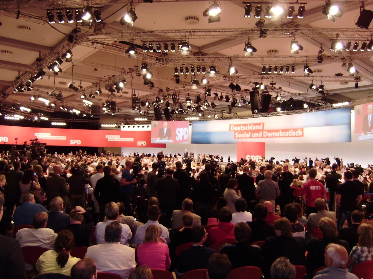 many people in a large room looking at several speakers