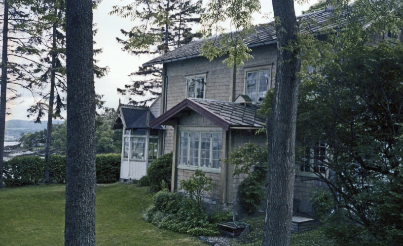 the house is next to the trees and has a gray roof