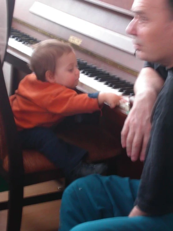 a man playing piano with his son in front of it