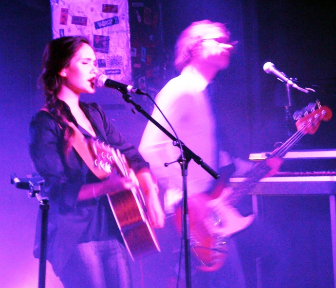 two people stand in front of microphones while playing guitars